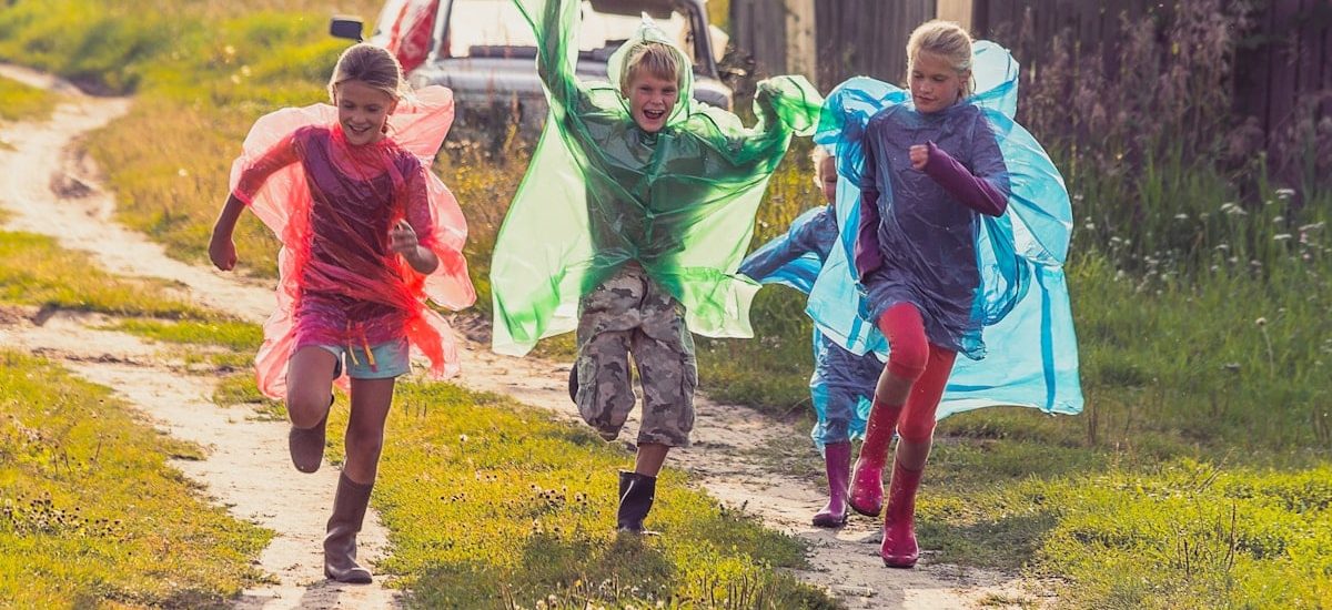 Group of kids in colorful raincoats run a race after the rain in the village