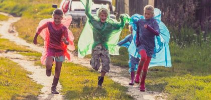 Group of kids in colorful raincoats run a race after the rain in the village