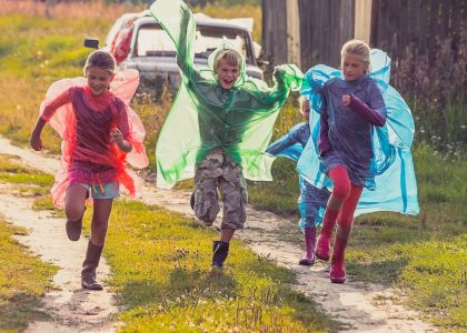 Group of kids in colorful raincoats run a race after the rain in the village