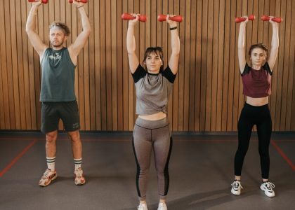 Three adults exercising with dumbbells in a gym setting, promoting fitness and healthy lifestyle.